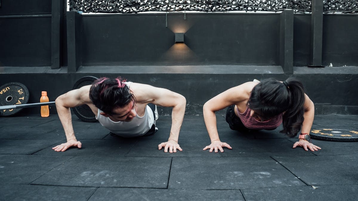 Two adults doing push-ups in an indoor gym setting in Mexico City, promoting a fit and healthy lifestyle.
